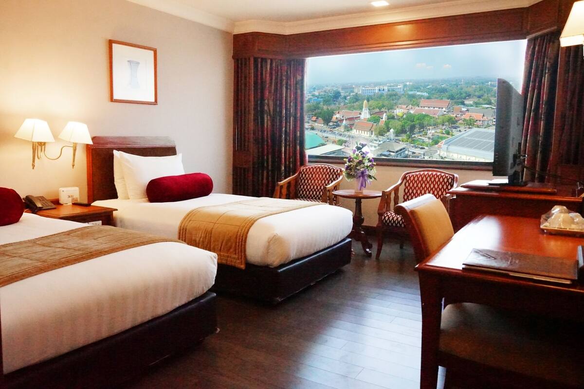 Habitación de hotel con dos camas, un escritorio, una silla, una mesita y vistas a la ciudad.