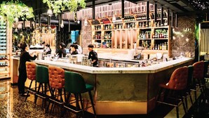 Una zona de bar con mostrador, taburetes y estantes llenos de botellas.