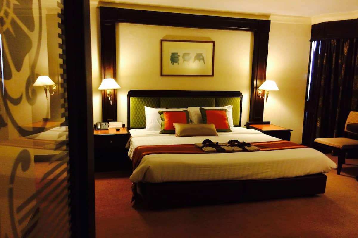 Habitación de hotel con una cama grande, dos mesitas de noche, un sillón y un cuadro en la pared.