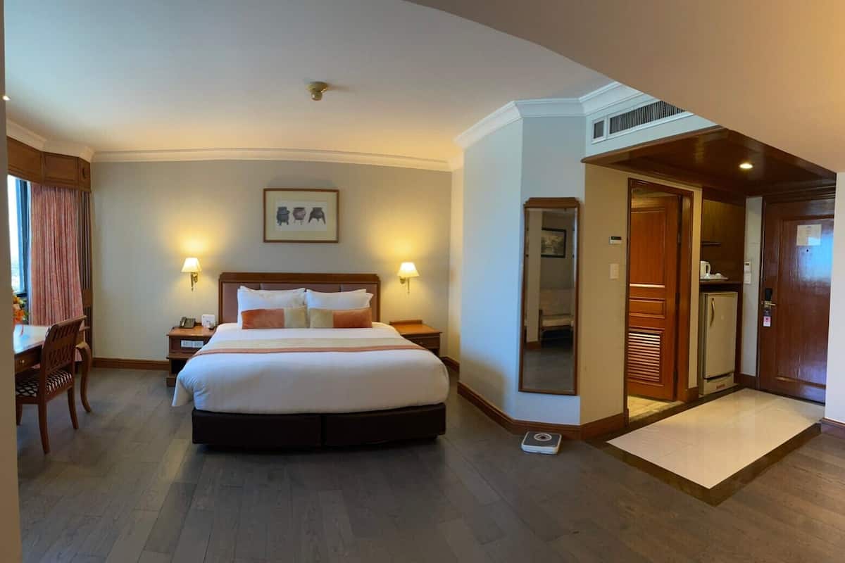 Una habitación de hotel con una cama grande, mesitas de noche, un escritorio y un espejo.