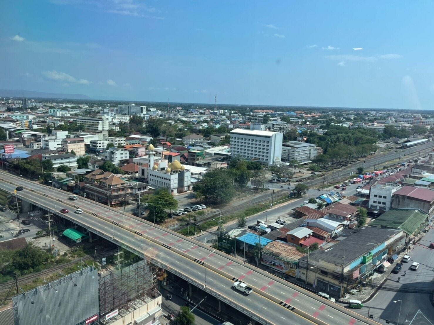 An aerial view of a cityscape with a prominent white building with multiple floors and a large golden dome, surrounded by various other buildings and a busy road with vehicles.