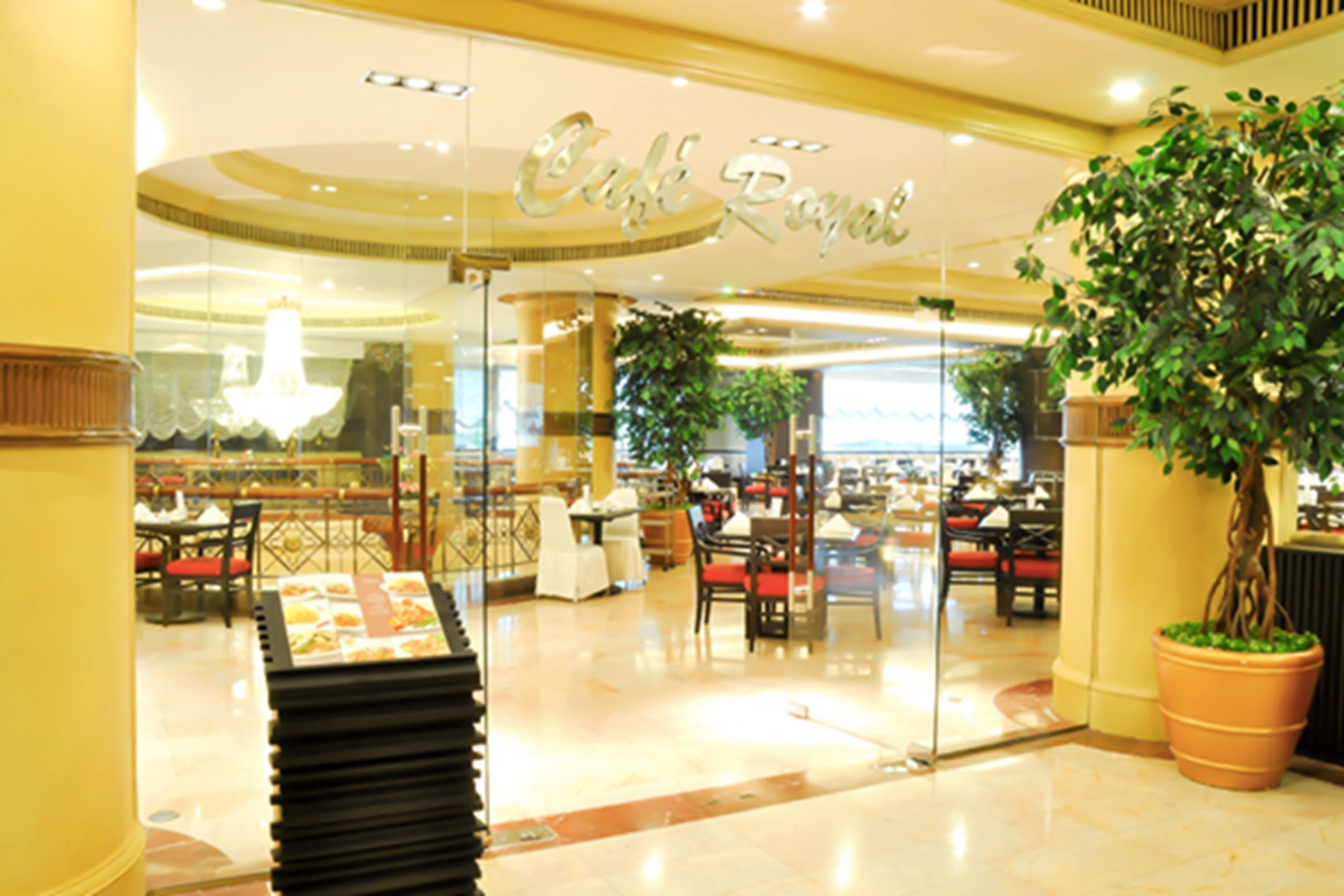 A restaurant with a glass entrance, indoor plants, and a sign that reads "Cafe Royal".