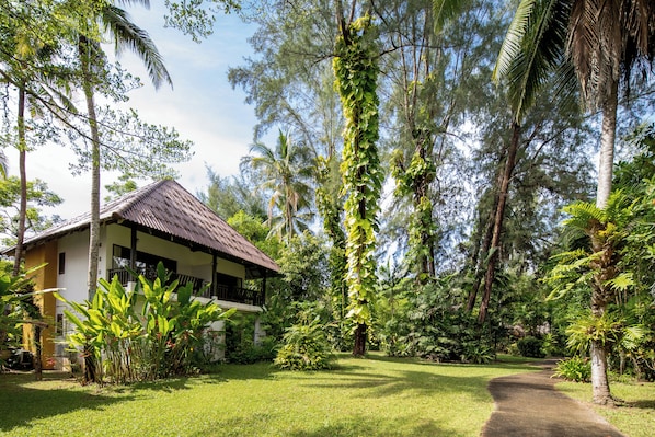 Un bungalow doté d’un toit de chaume, entouré d’une végétation luxuriante et accessible par un chemin dégagé menant à l’entrée.