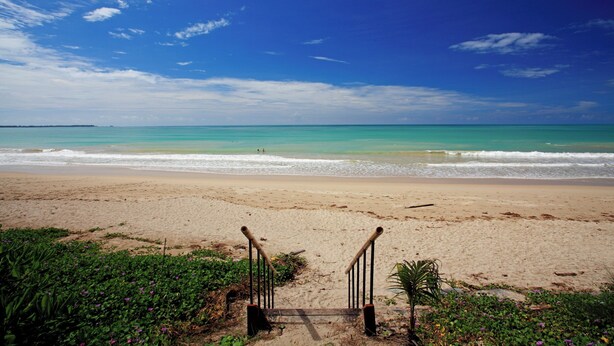 A beach with a wooden staircase leading to the shore, surrounded by greenery. - Haadson Resort (Takua Pa)