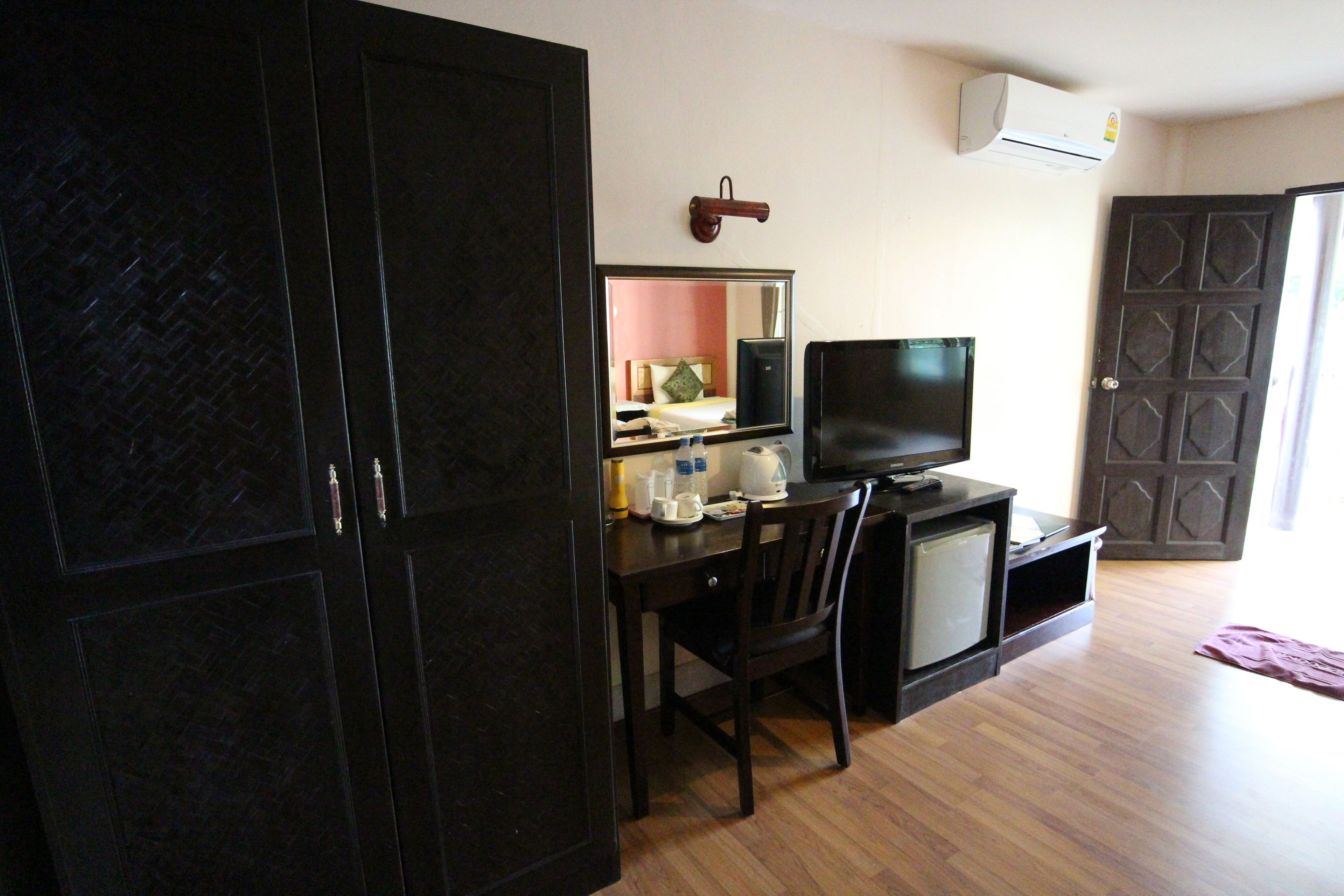 A room with a wooden desk, a television, a small refrigerator, and a mirror on the wall.