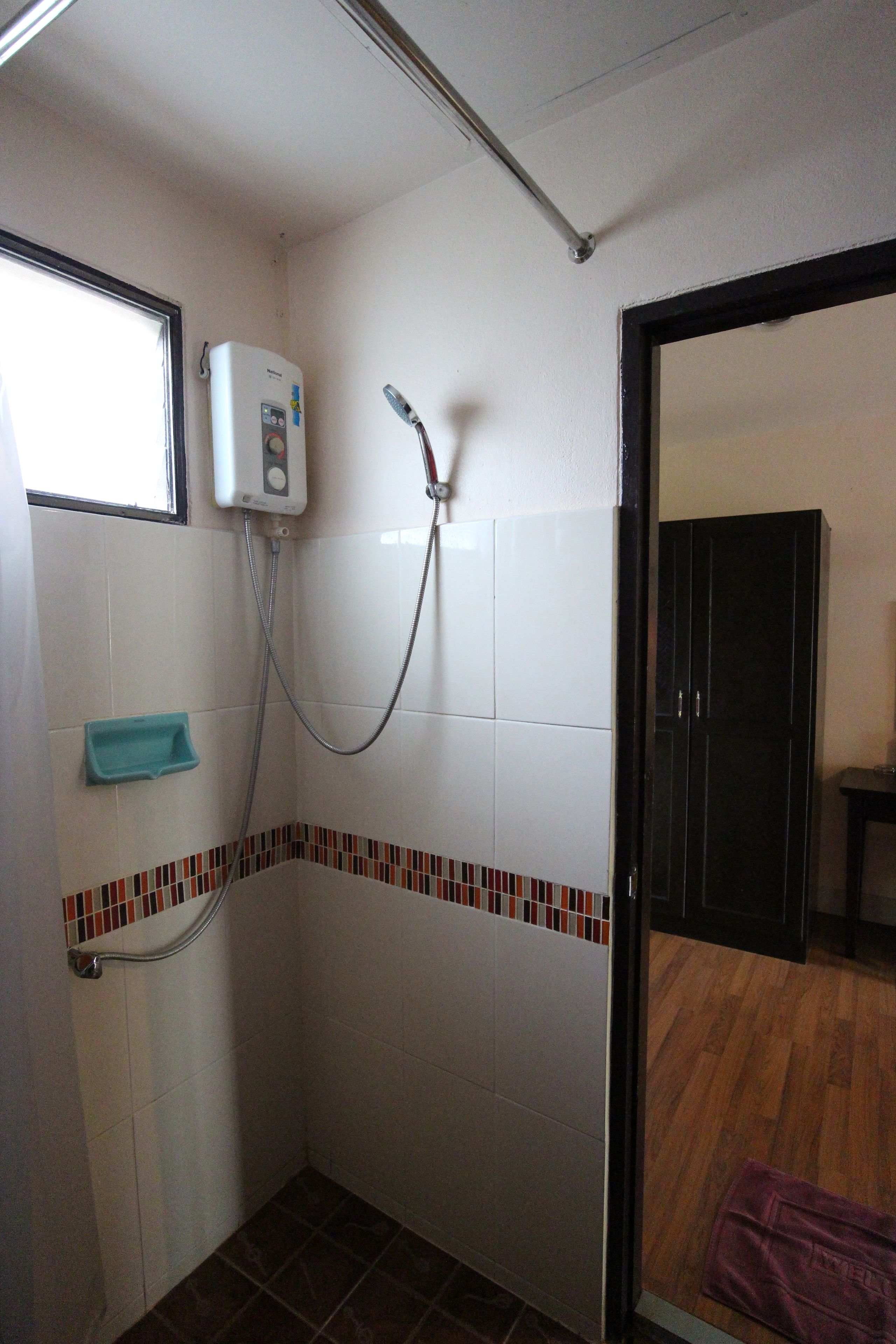 Un baño pequeño con azulejos blancos, una ducha, un ventanal y suelo de madera.