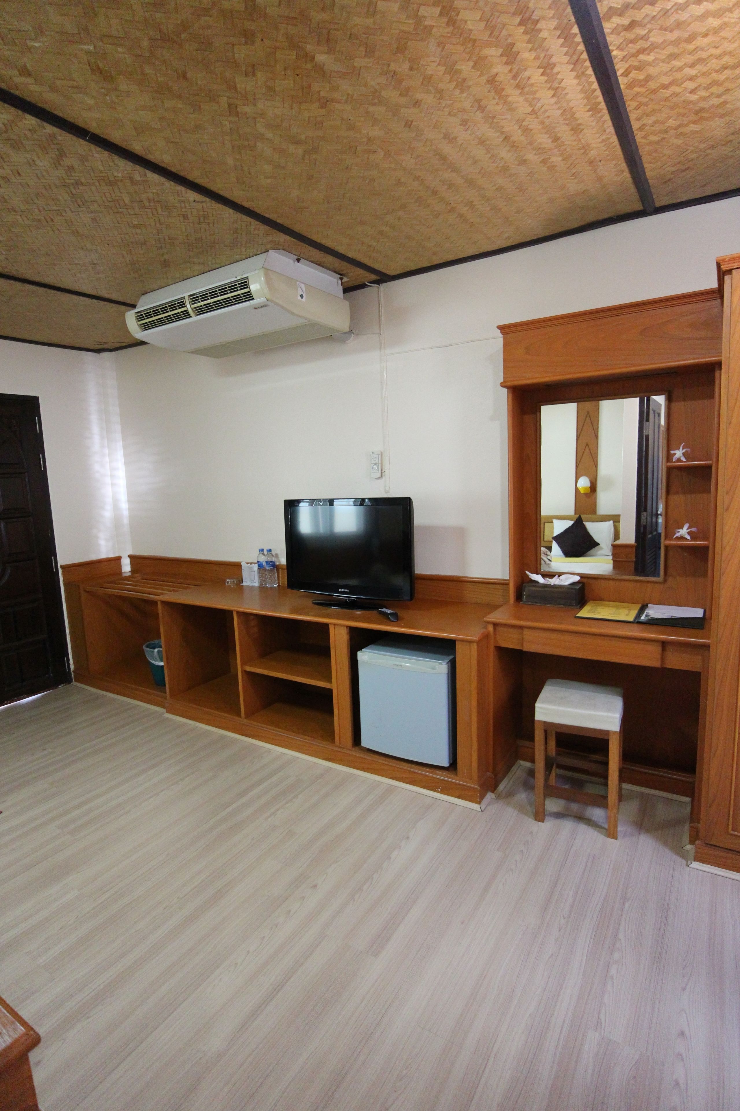 Una habitación con un escritorio de madera, televisión, refrigerador pequeño, armario de madera y un espejo.