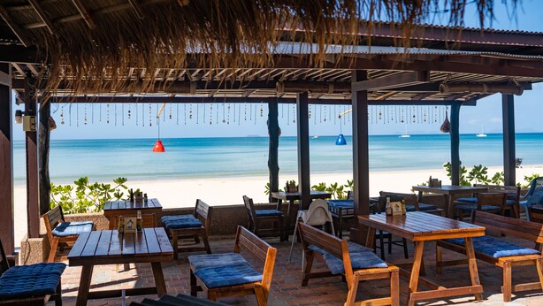 A beachside patio with wooden tables and benches, overlooking the ocean. - Southern Lanta Resort (Ko Lanta)