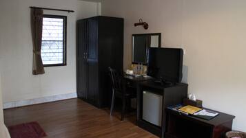 A compact room with a wooden floor, a desk with a computer and a television, a small refrigerator, and a chair.