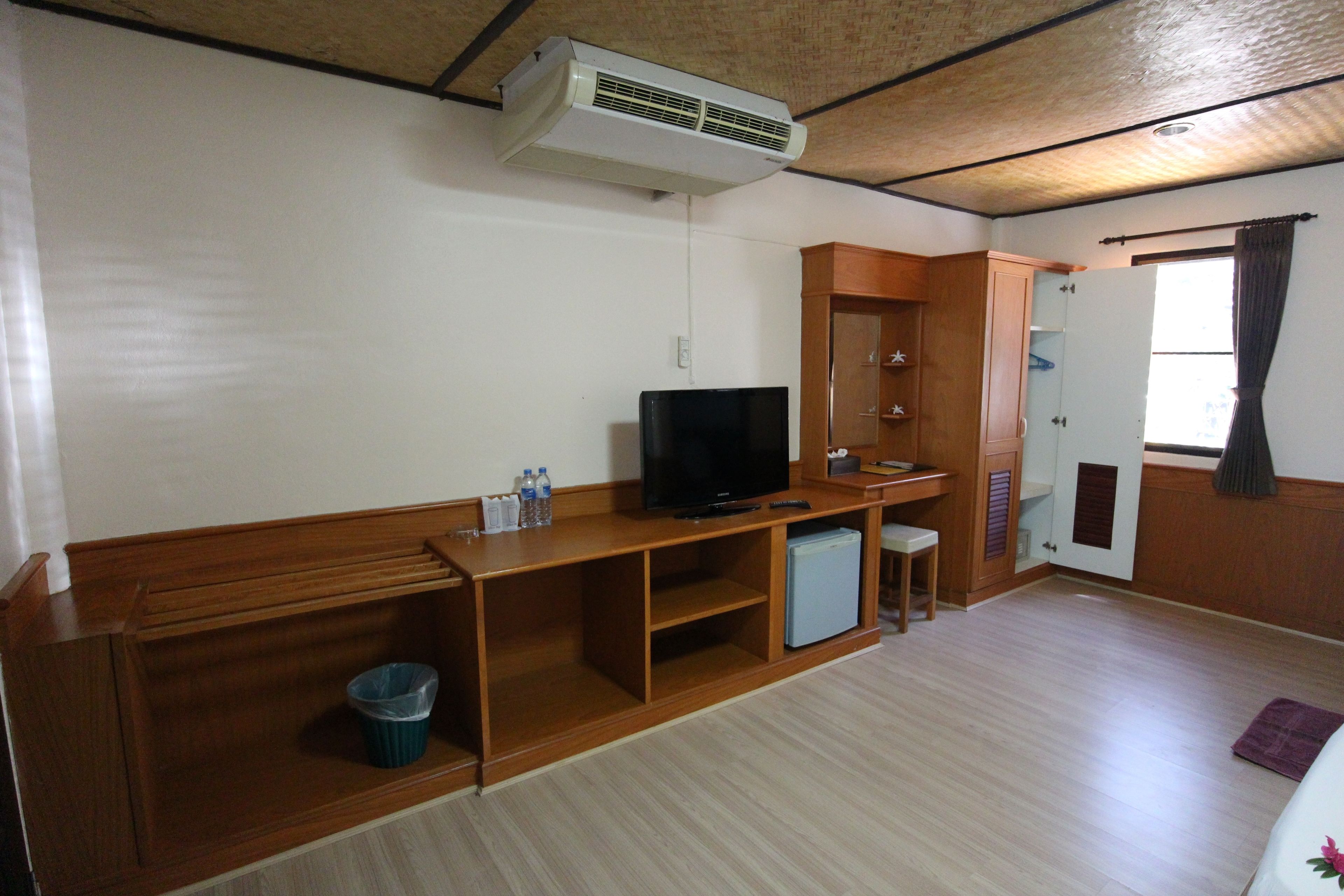 A room with a wooden cabinet, a television, a small refrigerator, and a trash bin.