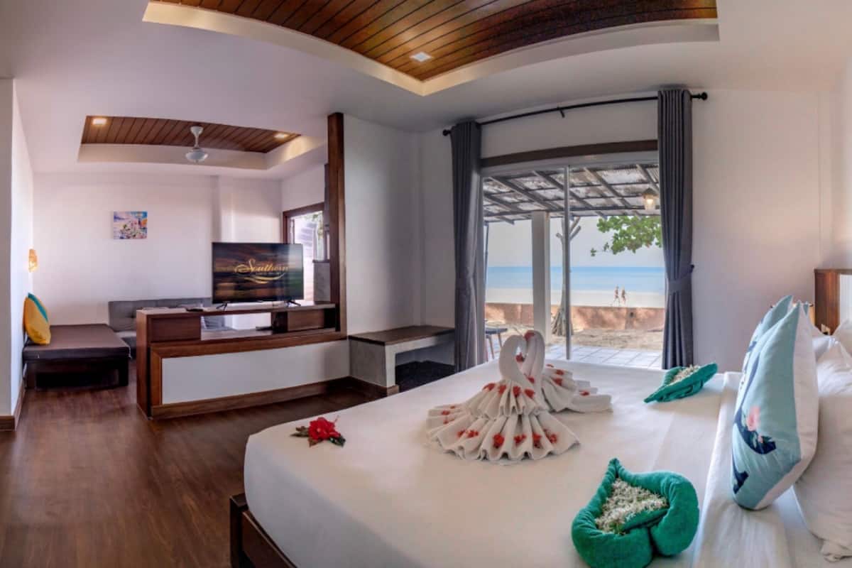 Ein Hotelzimmer mit Bett, Fernseher, Schreibtisch und Blick auf den Strand.
