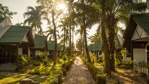 A pathway lined with palm trees and a brick walkway leading to a row of bungalow-style buildings with green roofs. - Southern Lanta Resort (Ko Lanta)