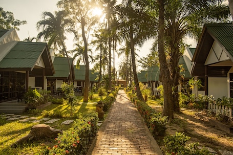 A pathway lined with palm trees and a brick walkway leading to a row of bungalow-style buildings with green roofs.