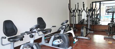 Un gimnasio con bicicletas estáticas, una máquina de remo y un espejo que refleja el equipo.