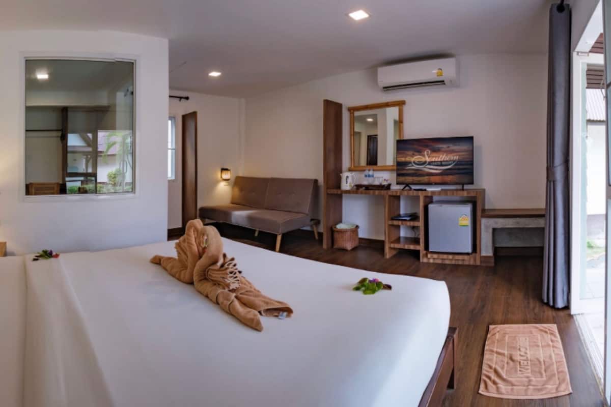 Ein Hotelzimmer mit einem großen Bett, einem Schreibtisch mit Computer, einem Sessel und einem Fernseher.