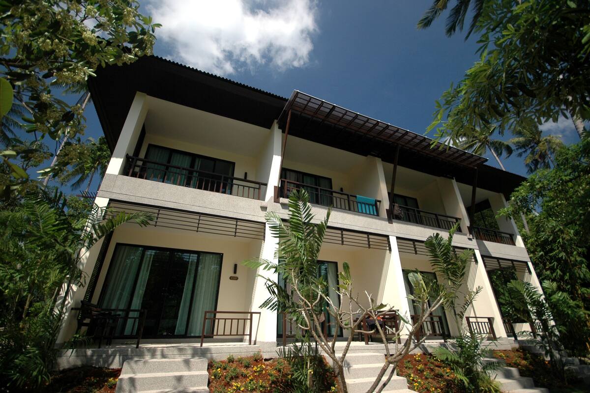 A multi-story hotel with balconies, large windows, and tropical landscaping.