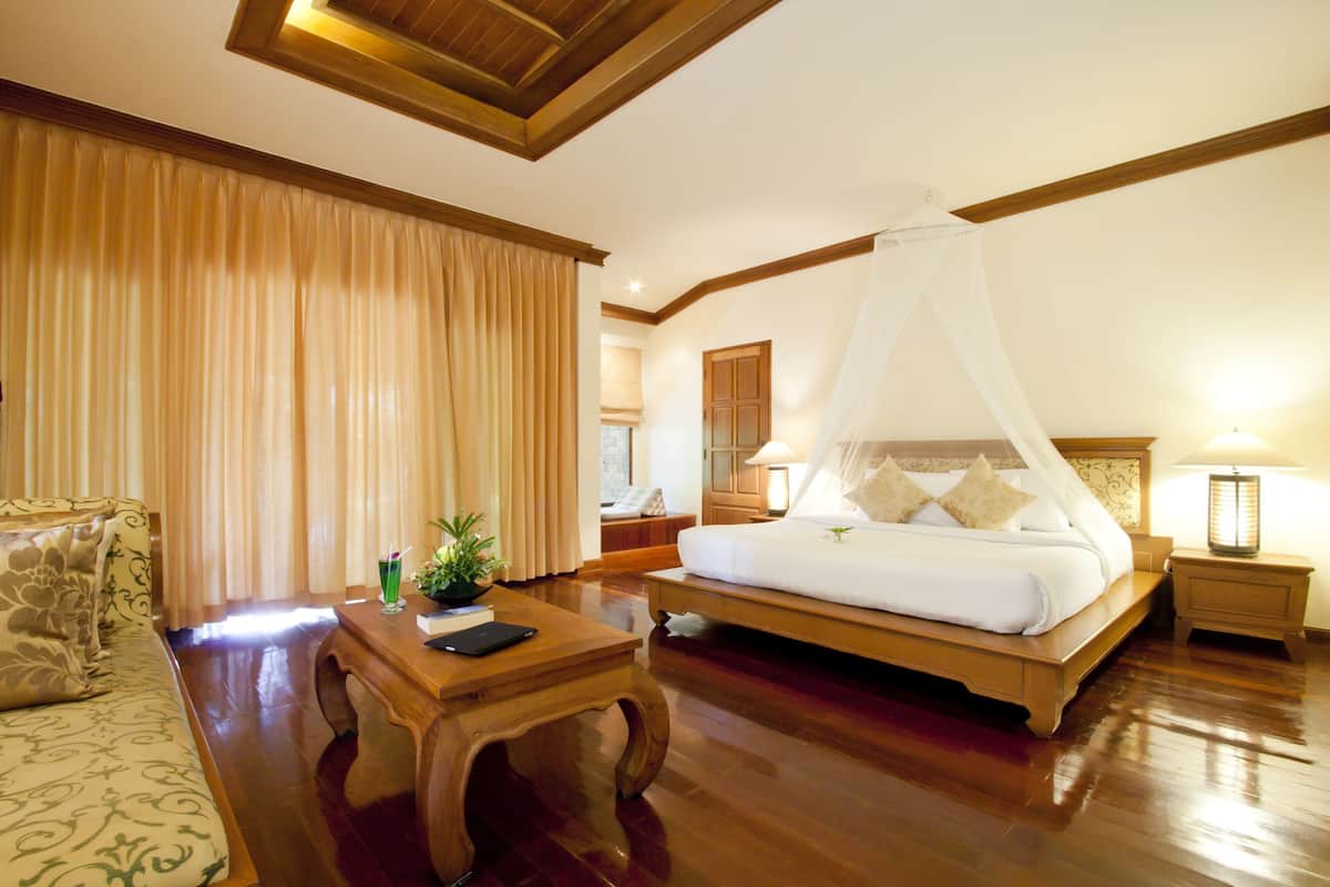 A hotel room with a wooden bed, a wooden nightstand, a wooden coffee table, and a sofa.
