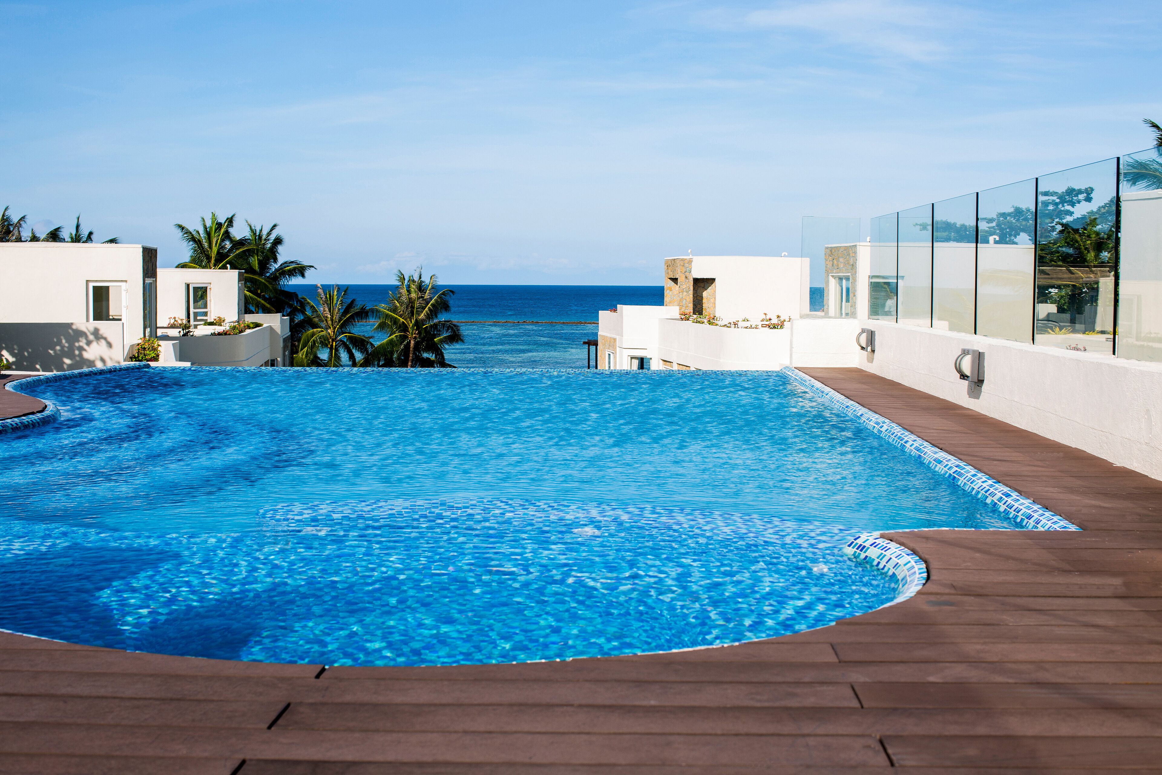 A swimming pool with a view of the ocean, surrounded by palm trees and modern architecture.
