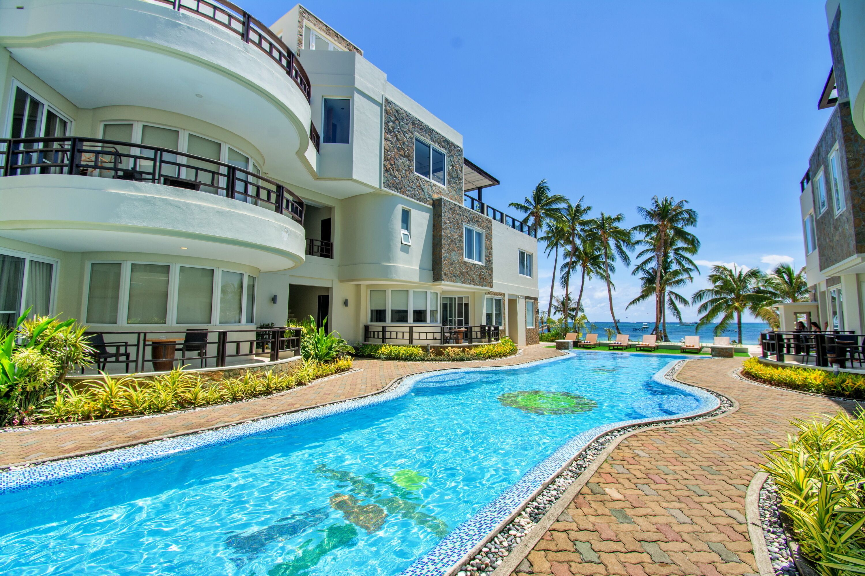 A hotel with a swimming pool, palm trees, and a view of the ocean.