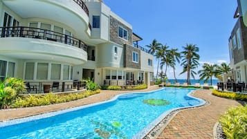 A hotel with a swimming pool, palm trees, and a view of the ocean.