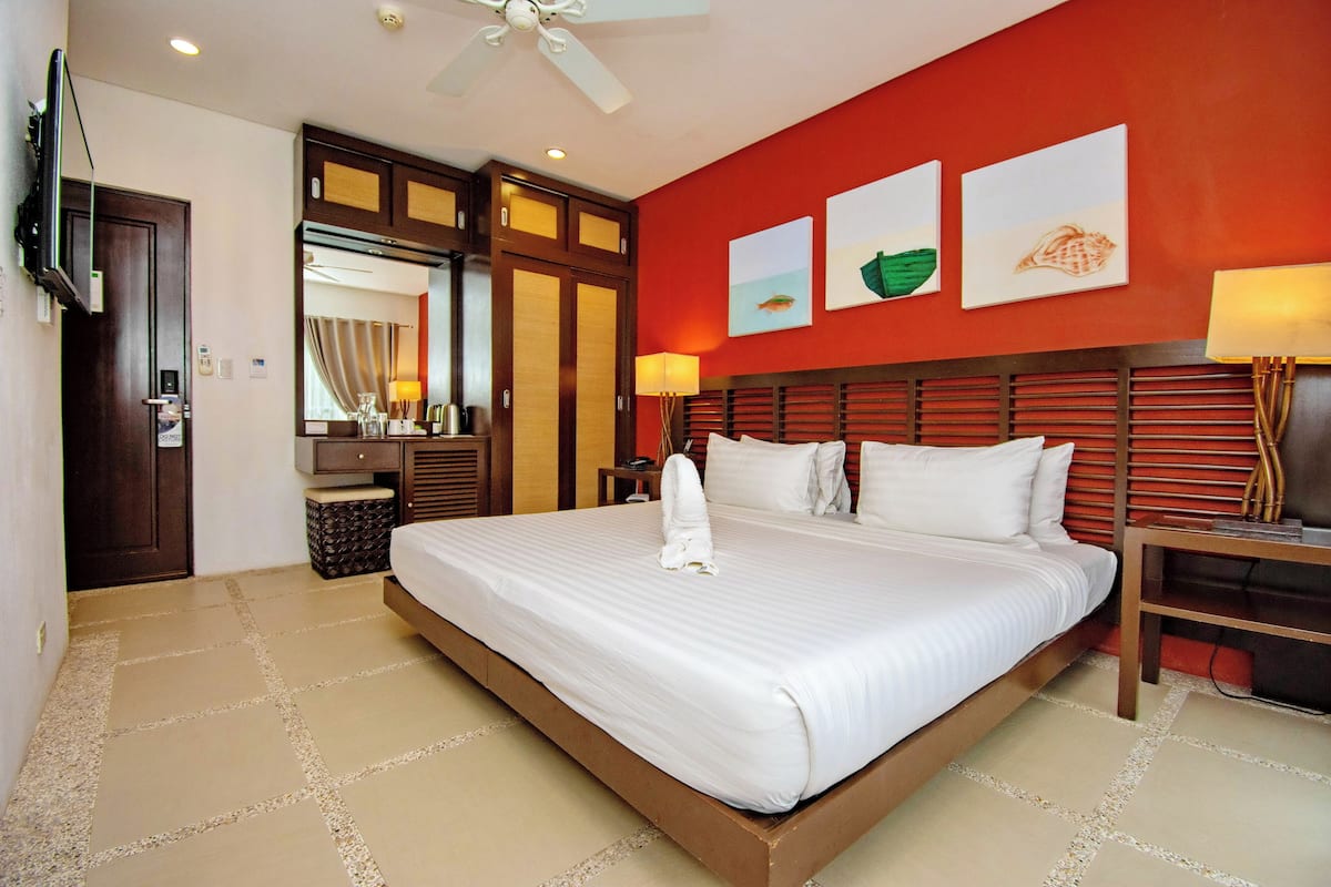 A hotel room with a large bed, a TV, a ceiling fan, and artwork on the wall.