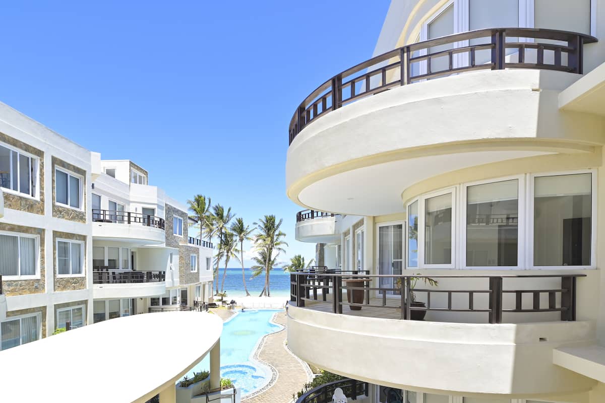 A multi-story hotel with balconies, a swimming pool, and a view of the beach.