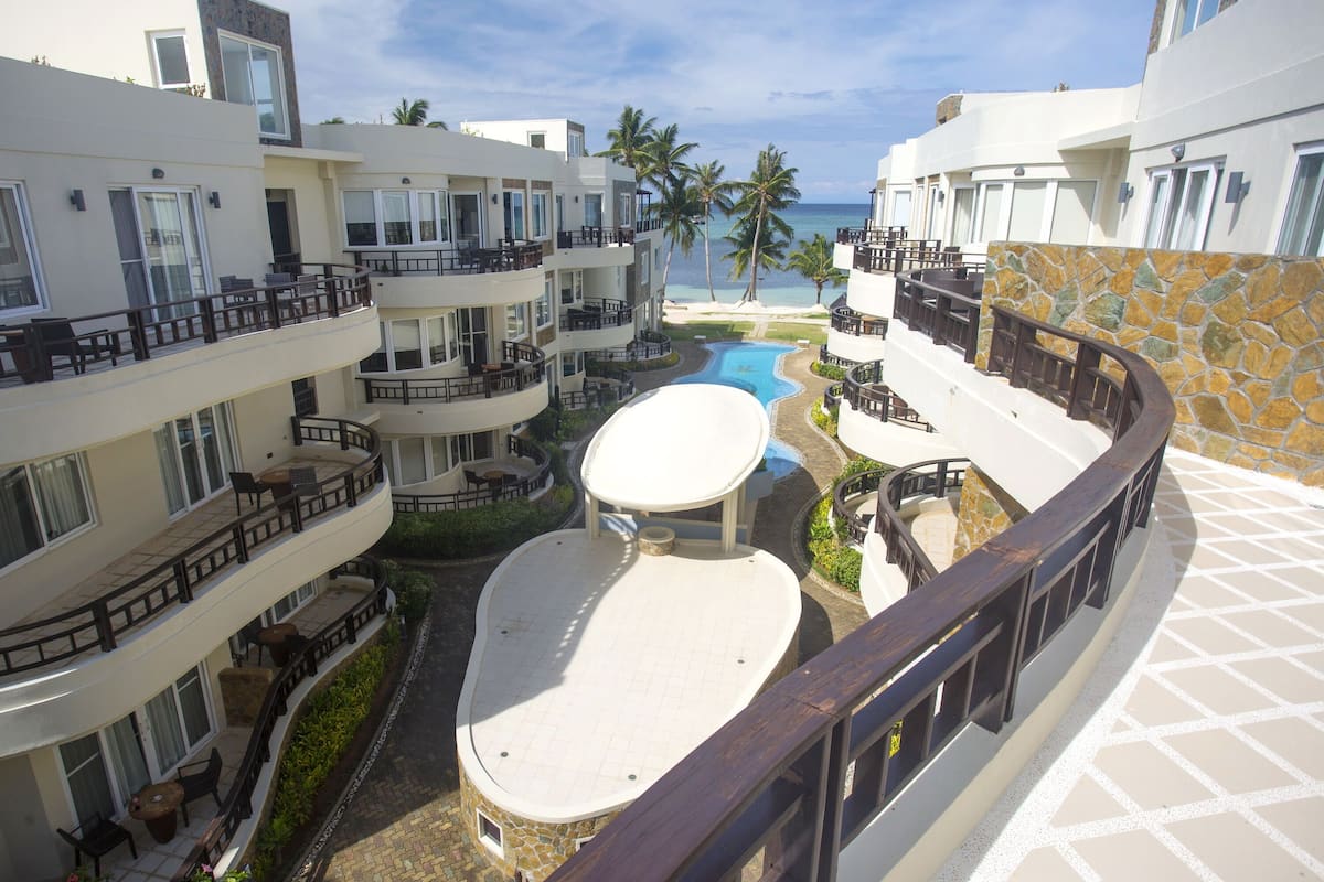 A resort with multiple balconies, a central swimming pool, and a view of the beach.