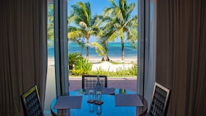 Ein Zimmer mit einem Glastisch, zwei Stühlen und Blick auf einen Strand mit Palmen und dem Meer.