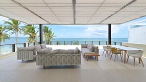 Ein geräumiger Balkon mit Blick auf den Ozean, möbliert mit einer Couch, Stühlen und einem Esstisch.