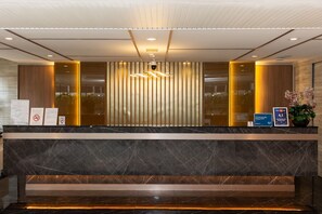 A hotel reception desk with a marble counter, vertical blinds, a modern chandelier, and informational signs. - Club Mahindra Mac Boutique Hotel  (Bangkok)
