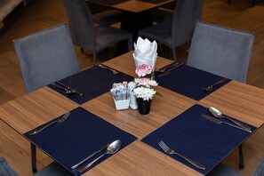 A dining table set with a vase of flowers, a small container of condiments, and cutlery. - Club Mahindra Mac Boutique Hotel  (Bangkok)