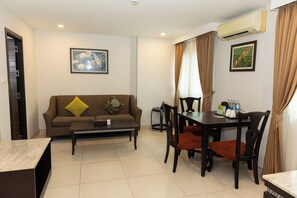 A furnished living room with a sofa, coffee table, dining table, chairs, and an air conditioning unit. - Club Mahindra Mac Boutique Hotel  (Bangkok)
