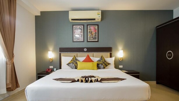 A hotel room with a large bed, two bedside tables, an air conditioning unit, and framed pictures on the wall. - Club Mahindra Mac Boutique Hotel  (Bangkok)