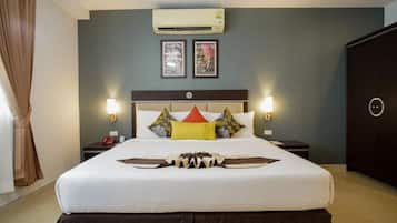 A hotel room with a large bed, two bedside tables, an air conditioning unit, and framed pictures on the wall.
