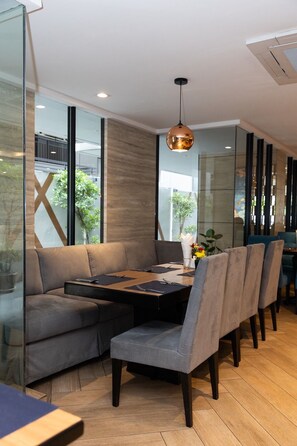 A modern dining area with a wooden table, grey upholstered chairs, and a pendant light. - Club Mahindra Mac Boutique Hotel  (Bangkok)
