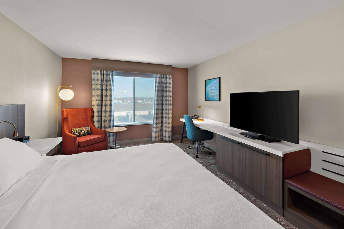 Une chambre d’hôtel comprenant un lit, un bureau avec une télévision, une chaise, une lampe de bureau et une fenêtre avec des rideaux.