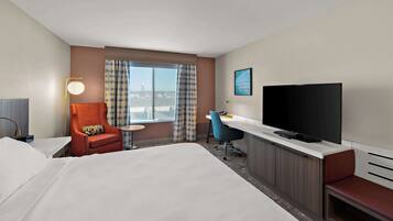 A hotel room with a bed, a desk with a TV, a chair, a desk lamp, and a window with curtains.