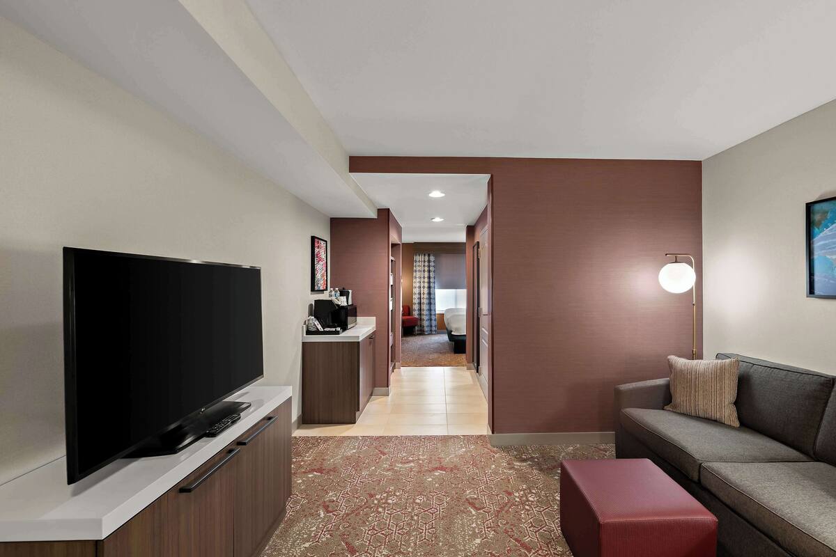 Un salon moderne doté d’un téléviseur à écran plat, d’un canapé, d’un pouf rouge et d’un couloir menant à une chambre.