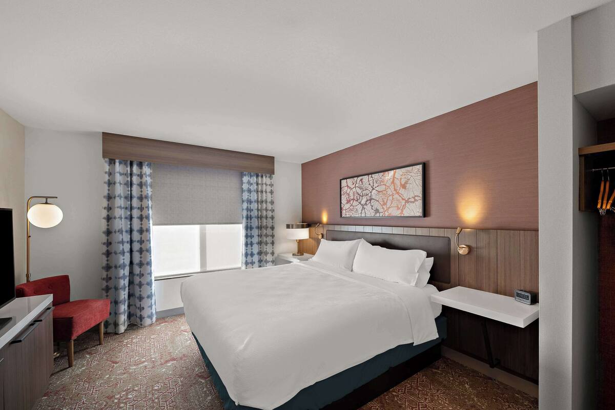 Une chambre d’hôtel avec un grand lit, des tables de chevet, un bureau, une chaise, une télévision et une fenêtre avec des rideaux.