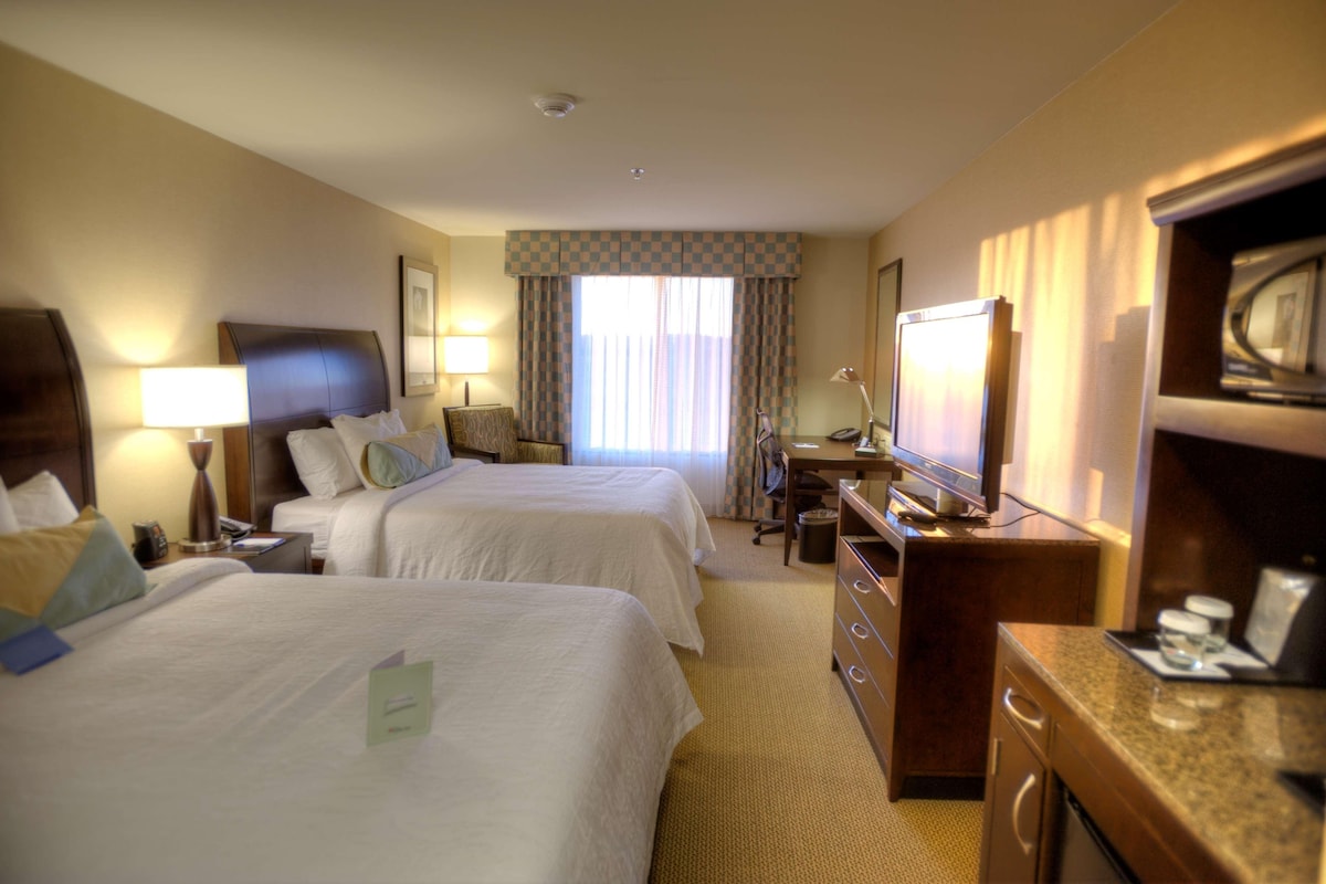 Habitación de hotel con dos camas, un escritorio, una silla, un televisor y un minibar.