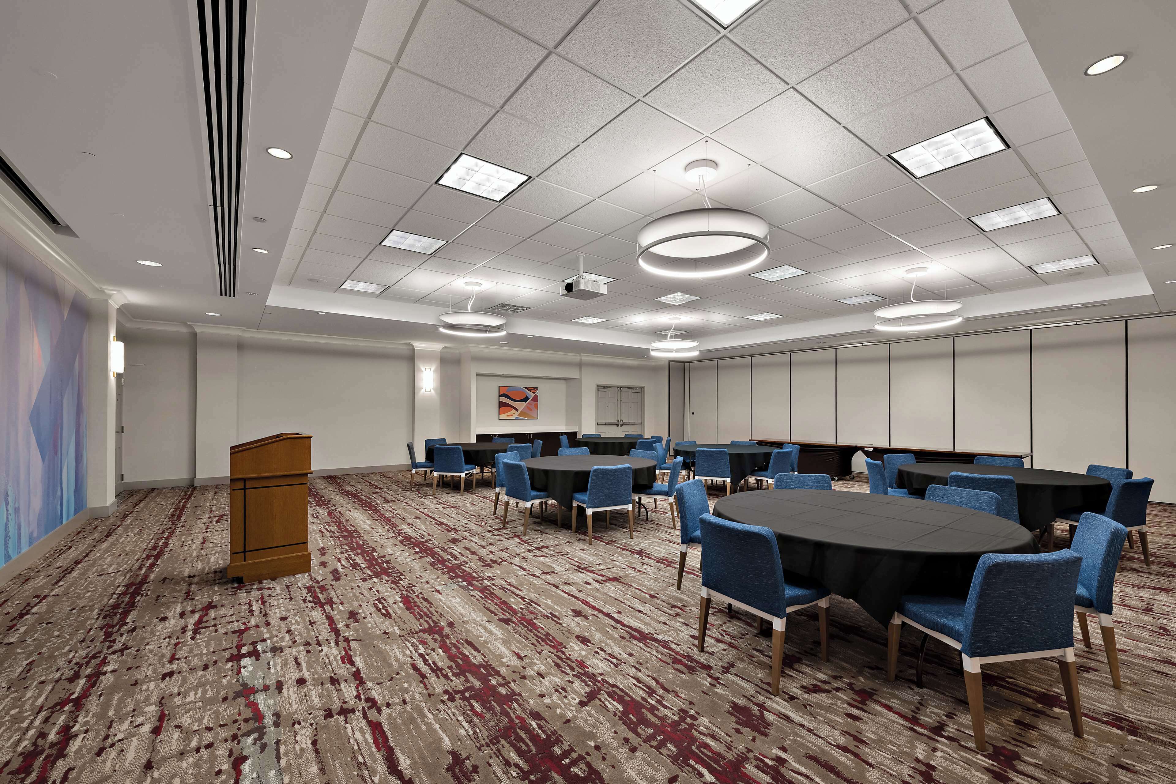 A conference room with a large table, blue chairs, and a podium.