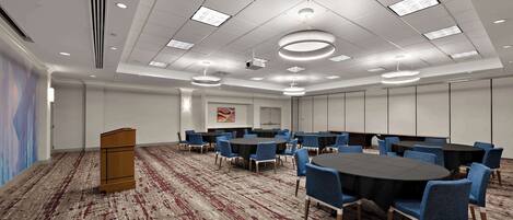 A conference room with a large table, blue chairs, and a podium.