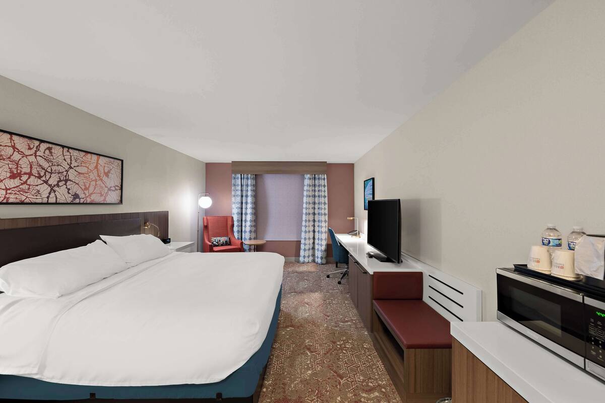 Une chambre d’hôtel dotée d’un grand lit, d’un bureau avec un téléviseur à écran plat, d’un micro-ondes et d’un coin salon comprenant une chaise et une petite table.