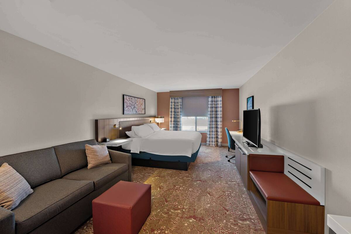 Une chambre d’hôtel avec un lit, un canapé, un bureau et une télévision.