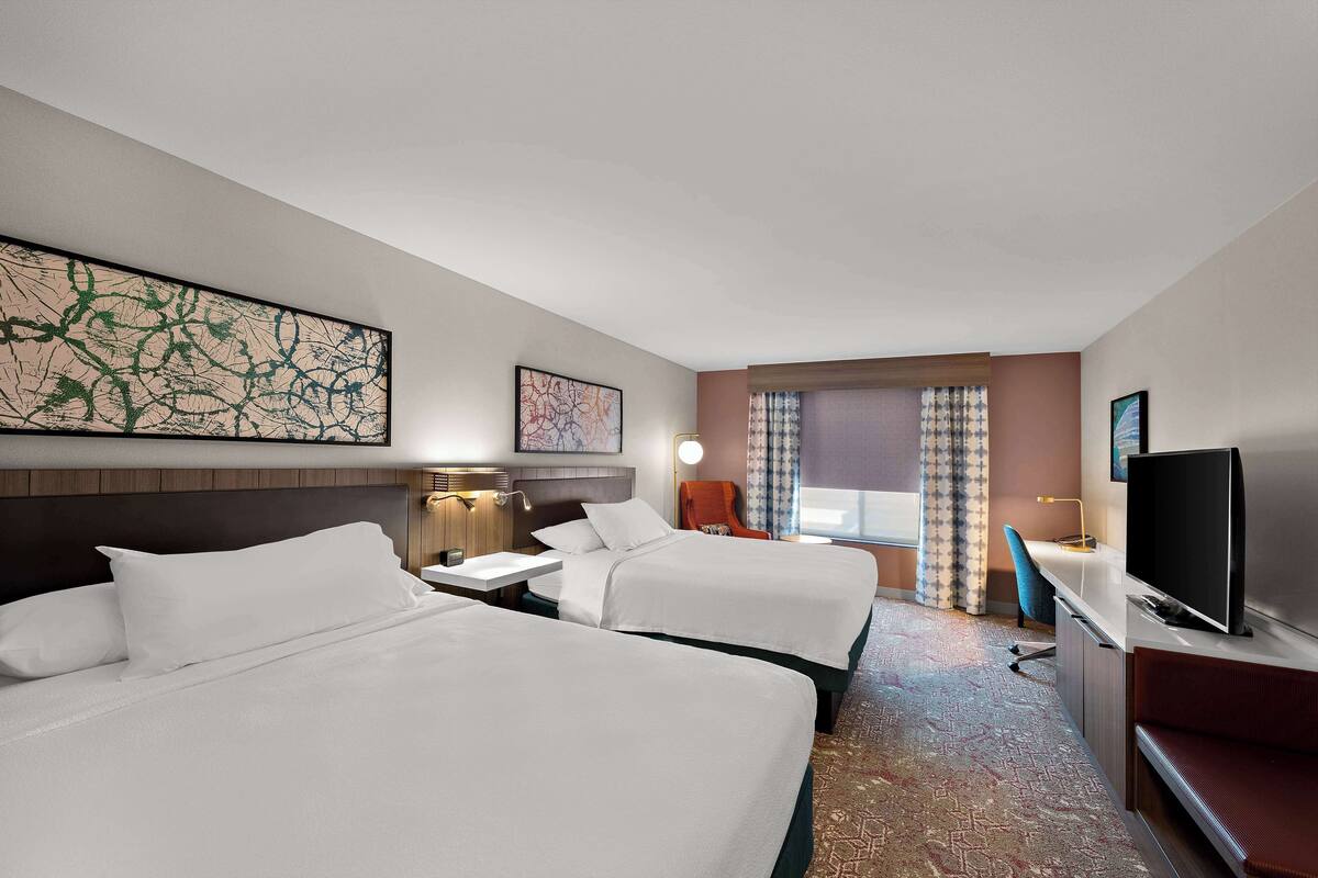 Une chambre d’hôtel avec deux lits, un bureau, une télévision et un grand tableau abstrait accroché au mur.