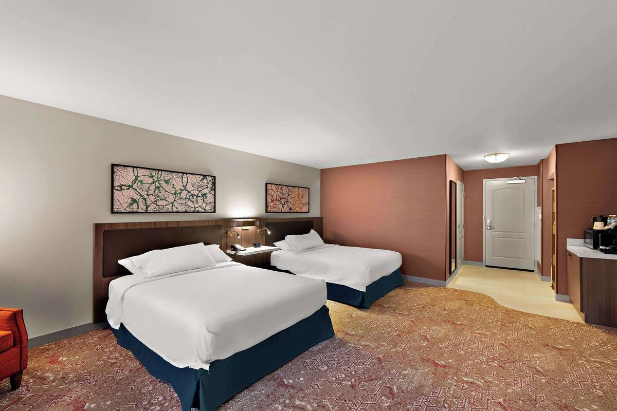 Une chambre d’hôtel avec deux lits, un bureau, une chaise et des œuvres d’art accrochées aux murs.