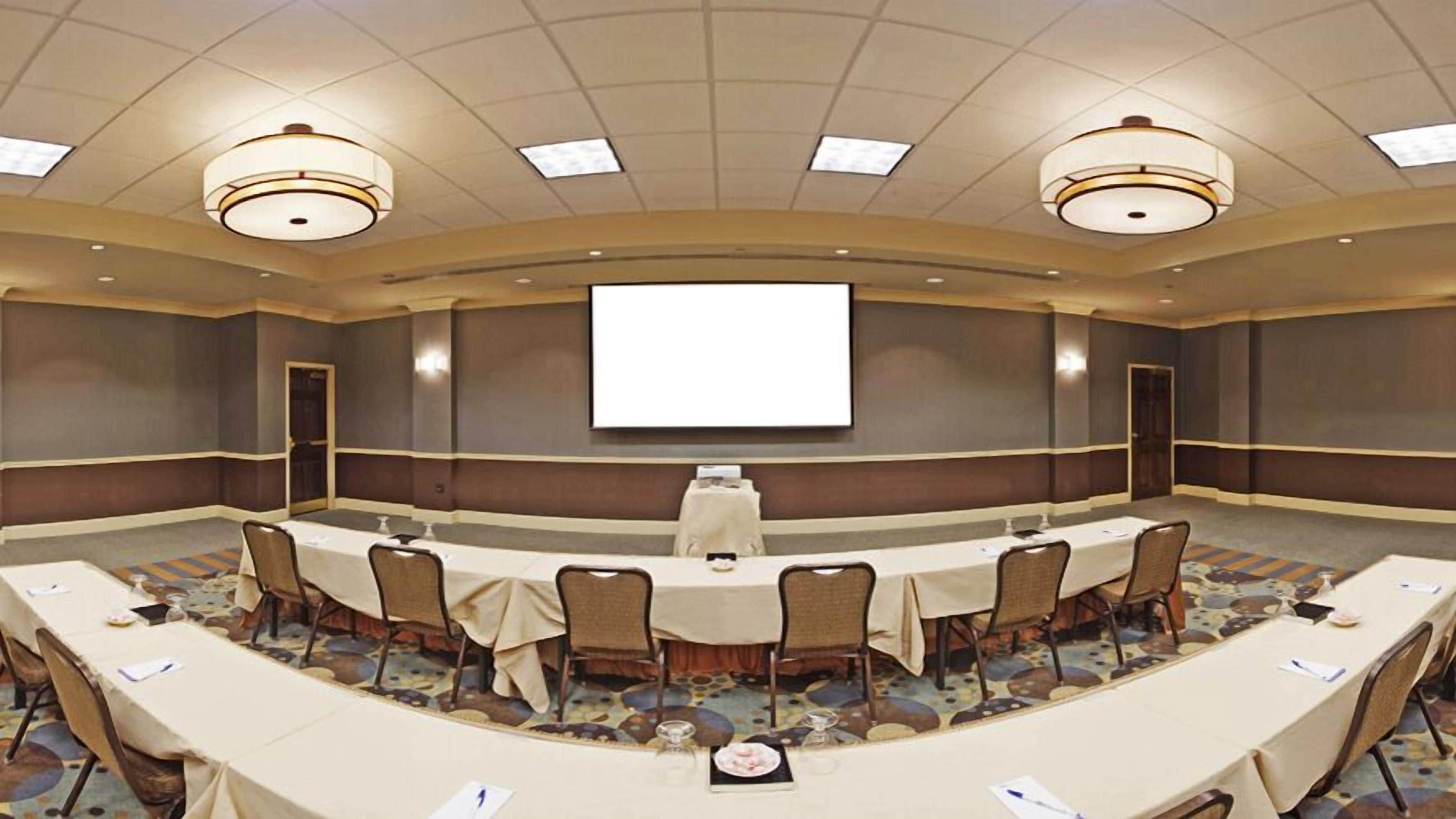 A conference room with a large screen, round tables, and chairs.