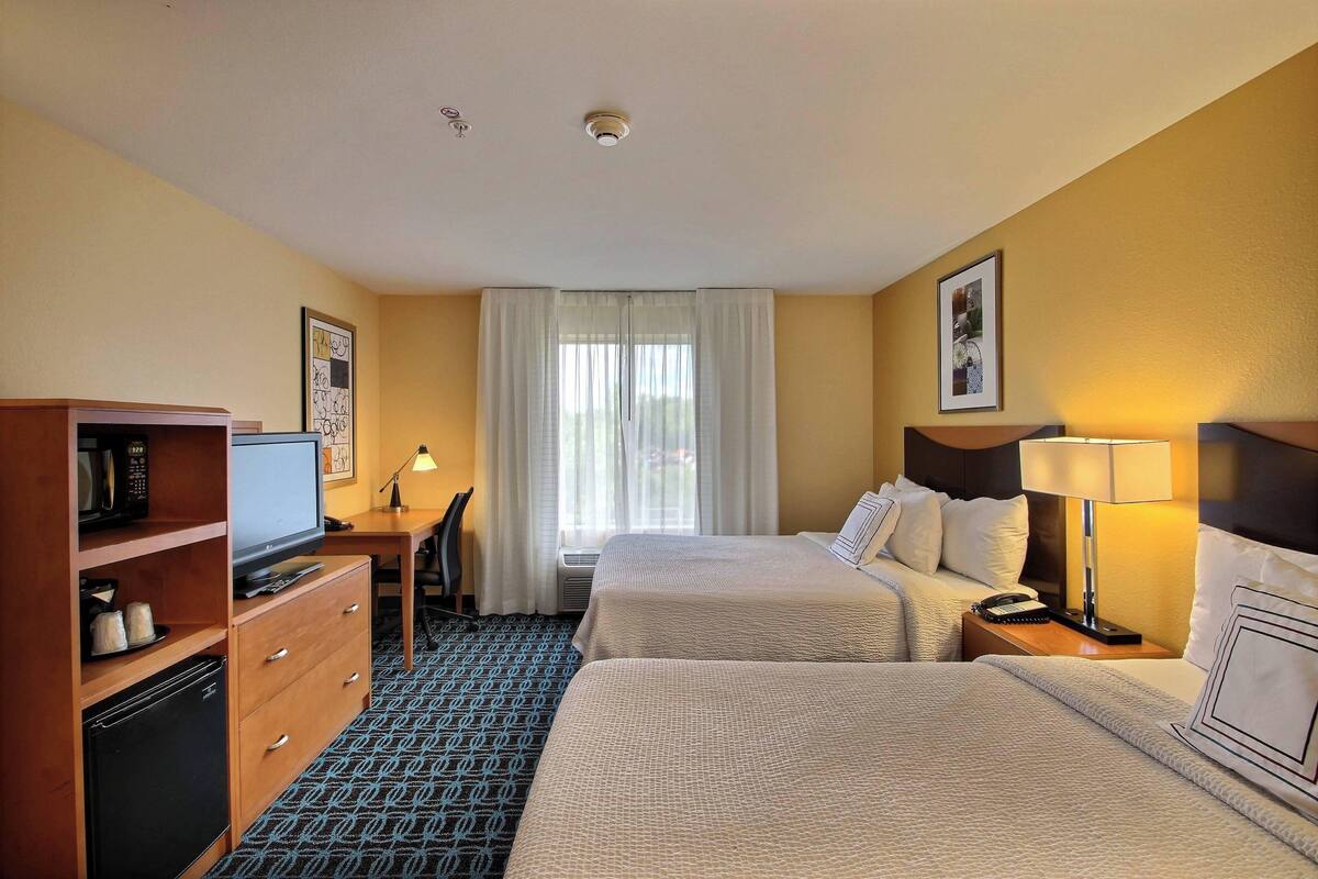 Une chambre d’hôtel avec deux lits, un bureau avec un ordinateur, un four à micro-ondes et un petit réfrigérateur.
