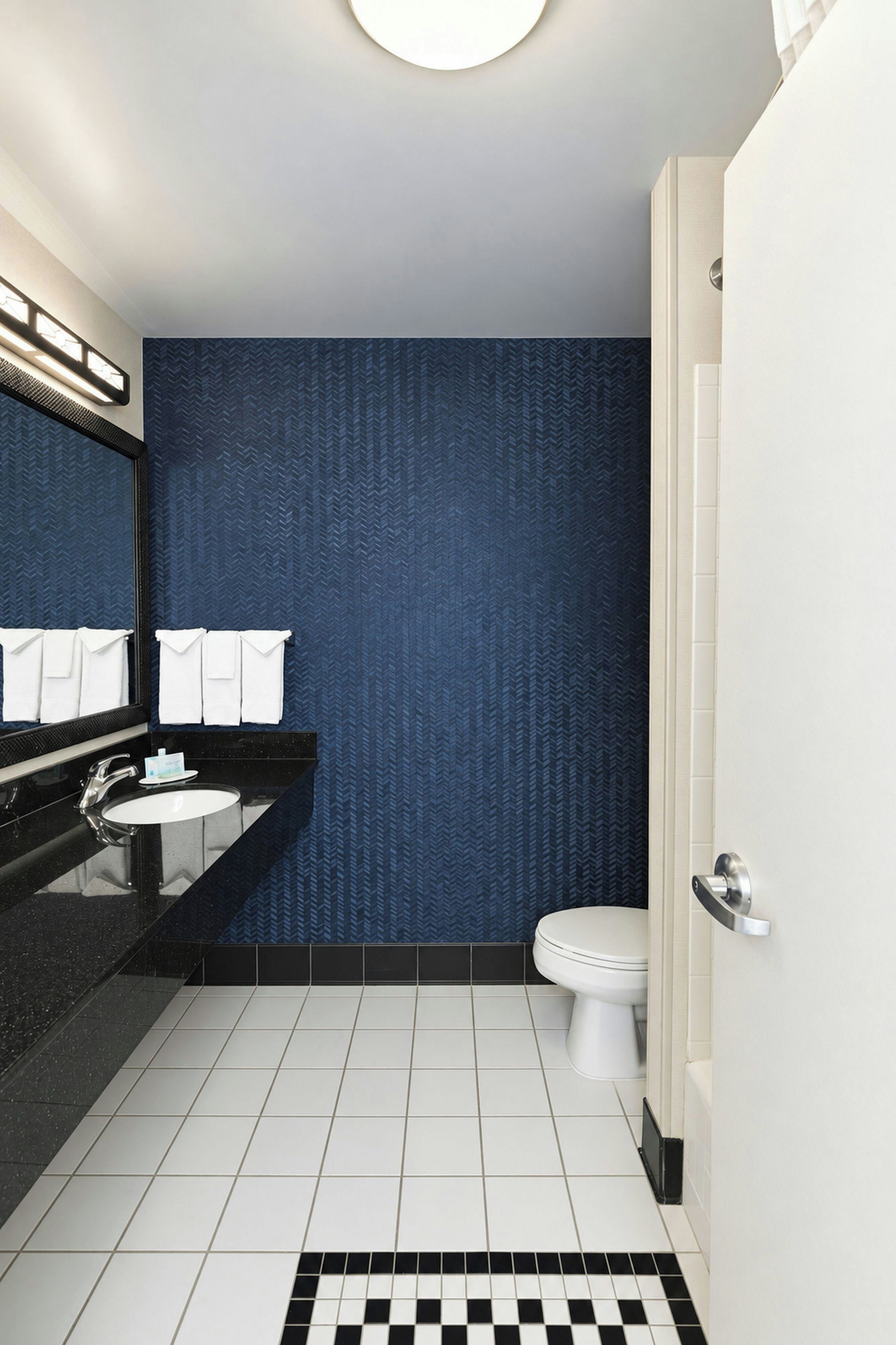 Une salle de bain moderne avec un lavabo noir, des toilettes blanches et un mur bleu à texture.