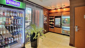 A corner market with a Naked beverage cooler, a Corner Market sign, and a refrigerator stocked with snacks. - Fairfield Inn & Suites by Marriott Milwaukee Airport (Oak Creek)